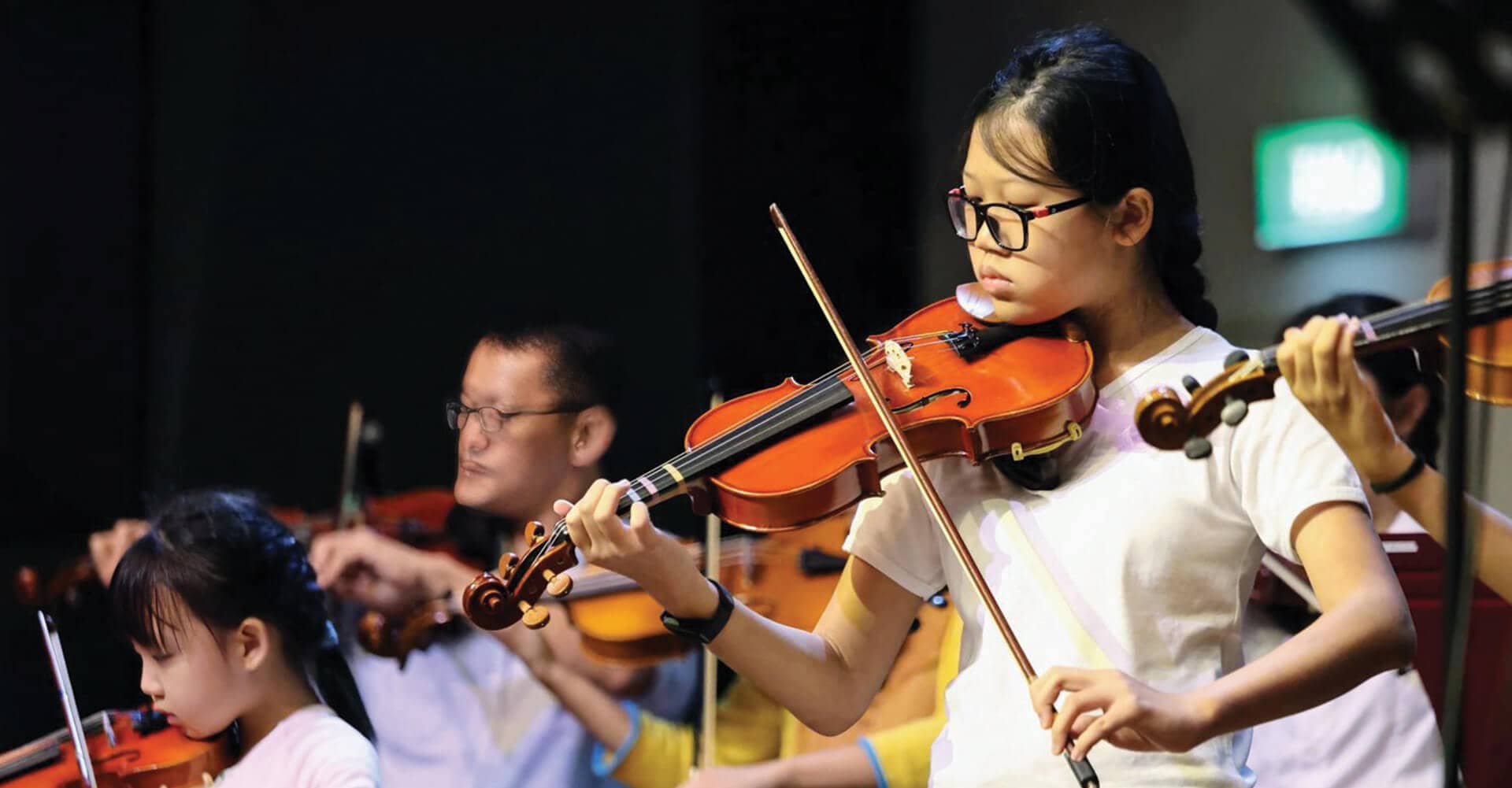 Students and adults performing in a violin ensemble at the Methodist School of Music, showcasing multi-generational learning and musical excellence in Singapore