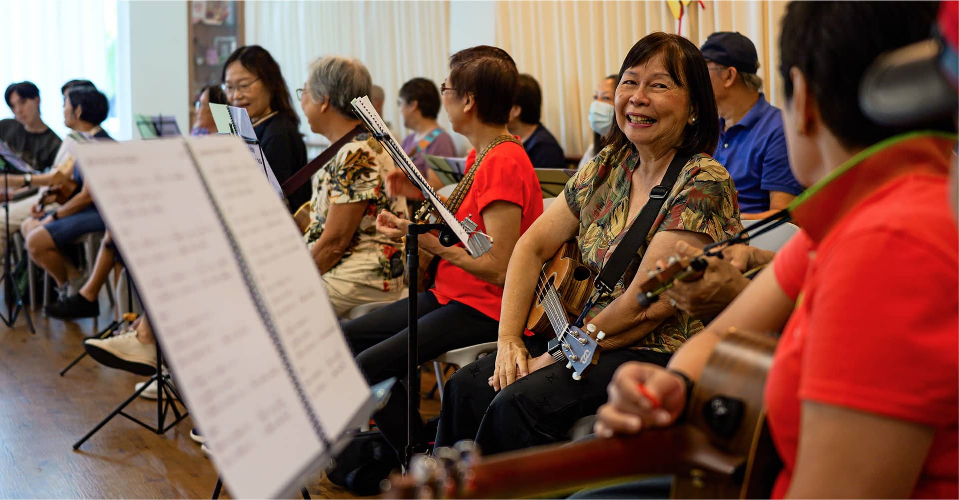 Senior adults participating in a joyful ukulele group session at the Methodist School of Music, Singapore, promoting community engagement through music education.