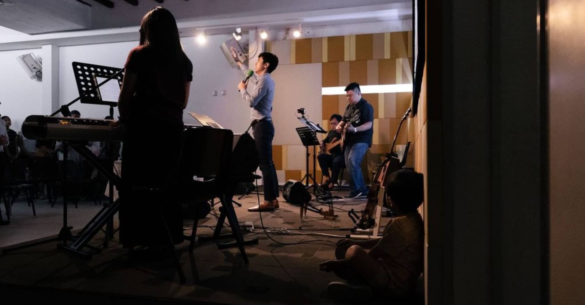 Live worship band performing at a church service led by the Methodist School of Music, with musicians on keyboard, guitar, and vocals, and a congregation in attendance.